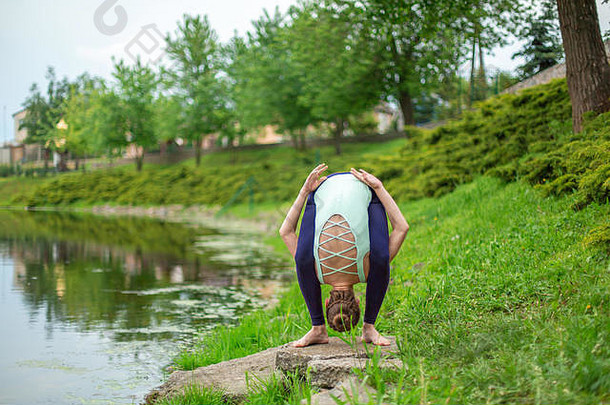 年轻的体育女孩实践瑜伽绿色草坪上河阿三的姿势团结自然