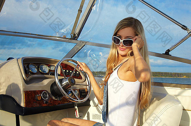 年轻的美丽的金发女郎太阳镜游艇的操舵轮