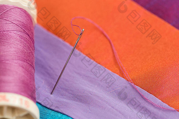 线程通过针眼睛特写镜头橙色背景线圈紫罗兰色的线程色彩斑斓的织物宏生产拼接而成被子手工制作的