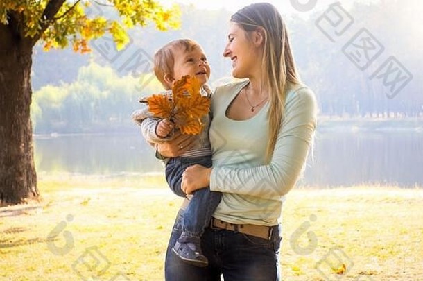 <strong>在</strong>秋天公园，一位年轻的母亲微笑着拥抱着她的小儿子