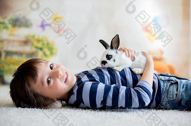 可爱的蹒跚学步的小男孩，穿着时髦的休闲装，在家里和小黑白兔玩耍