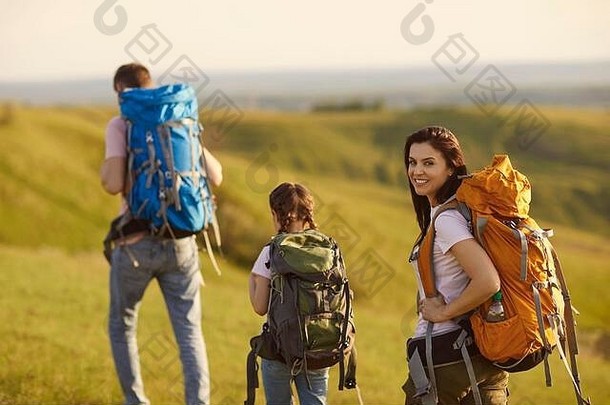 夏天，背着背包的旅行者一家人在大自然的山间草地上散步。