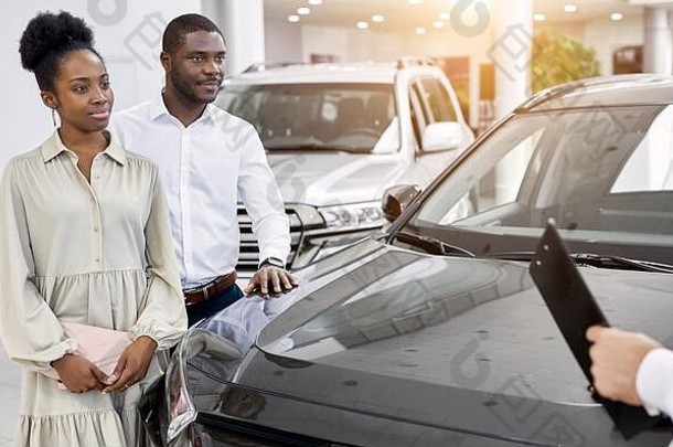 英俊的年轻汽车推销员向非洲夫妇讲述汽车的特点，美丽的已婚夫妇选择汽车