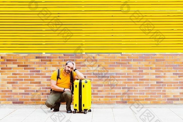 一个穿着橙色衬衫的男人拿着一个手提箱等在街上的地板上