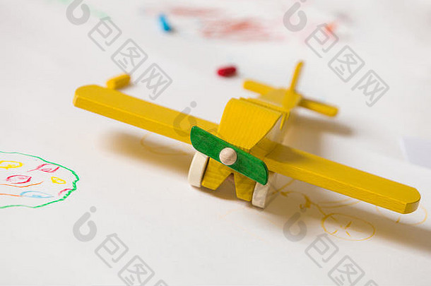 白色背景上的黄色木制玩具飞机。教育，孩子，游戏观念。孩子们用玩具画画。童年快乐的快乐幼儿园。