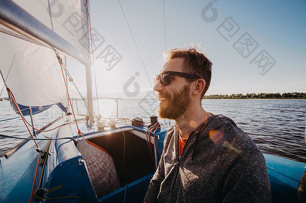 一名男子穿着休闲服，戴着墨镜在游艇上。留着胡子的快艇手成人近景照。船上英俊的水手在海上或河流上的<strong>盛典</strong>中微笑。