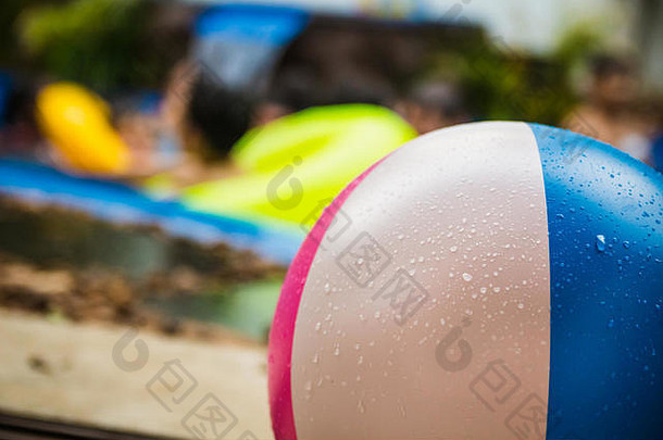 游泳池里五颜六色的湿沙滩球的特写镜头。背景模糊，人们在水里玩得很开心。