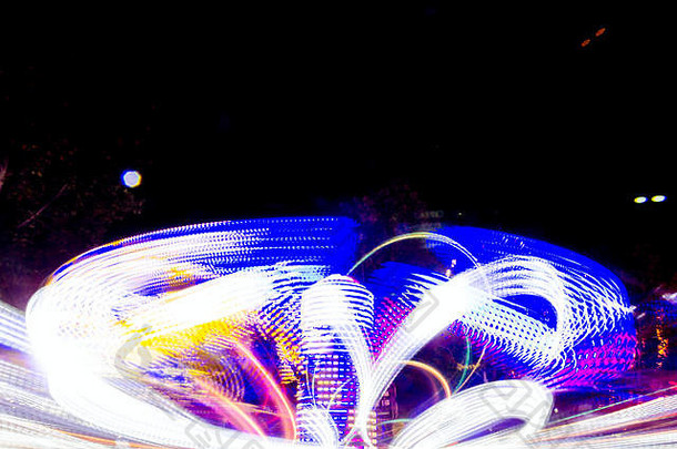 一个快速旋转的彩色旋转木马的长时间曝光，在夜晚用生动的灯光照亮，在月球公园的游乐场骑行。