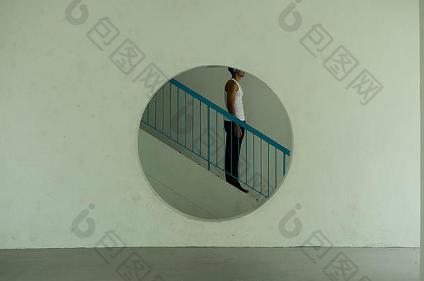一个现代年轻人站在楼梯上，穿过水泥墙上的一个圆圈，这是一张很酷的时尚照片