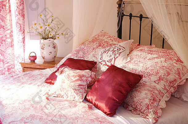 粉色丝绸靠垫，配有粉色绒布绗缝靠垫，黄铜床上有配套的床罩，白色的薄纱窗帘