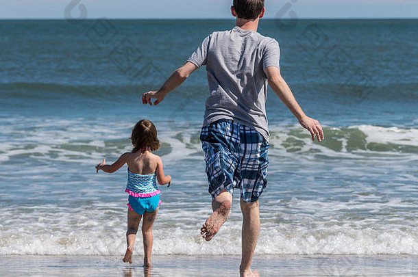 父亲和小女儿在海浪中奔跑的后视图