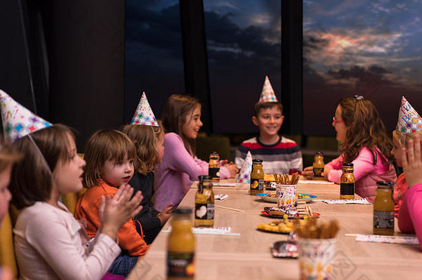 年轻的快乐男孩和他的朋友们正在举行生日聚会，背景是透过窗户的夜空