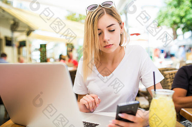 深思熟虑的女人持有电话移动PC电脑在线沟通喝cockail阳台咖啡馆
