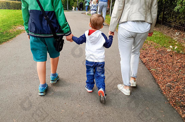 照片蹒跚学步的男孩持有妈妈。老哥哥手走秋天公园