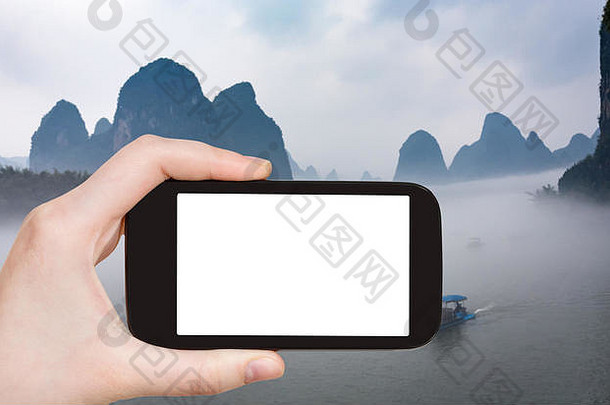 旅游理念——春天的早晨，游客用智能手机在阳朔县兴平镇附近的河面上拍摄雾中的船只