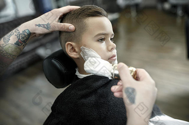 儿童理发师在黑暗的背景下给小男孩理发。心满意足的可爱学龄前男孩正在理发。