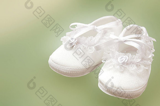 绿色背景上洗礼用白色婴儿鞋。