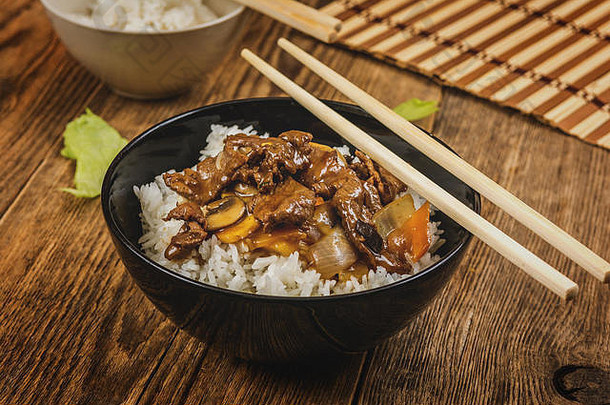黑盘子和筷子上的亚洲牛肉配蔬菜和米饭