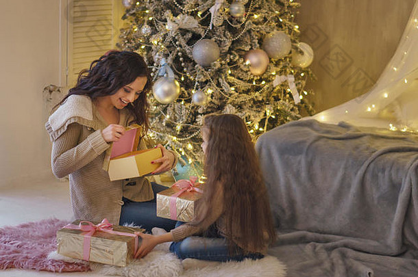 家庭庆祝活动妈妈。女儿坐着圣诞节树持有礼物女人打开礼物喜乐快乐童年