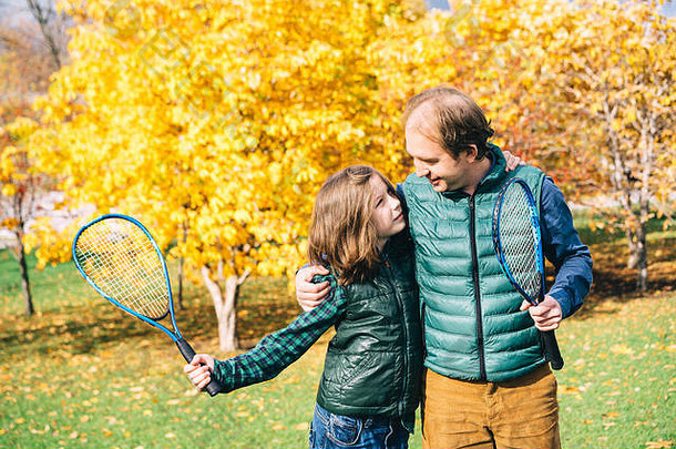 父亲和儿子在秋天的公园里玩网球拍