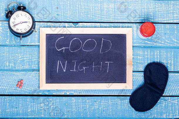 “睡眠概念”展示了一个闹钟、安眠药、眼罩和一块黑板，在风化的蓝色背景上写着“晚安”
