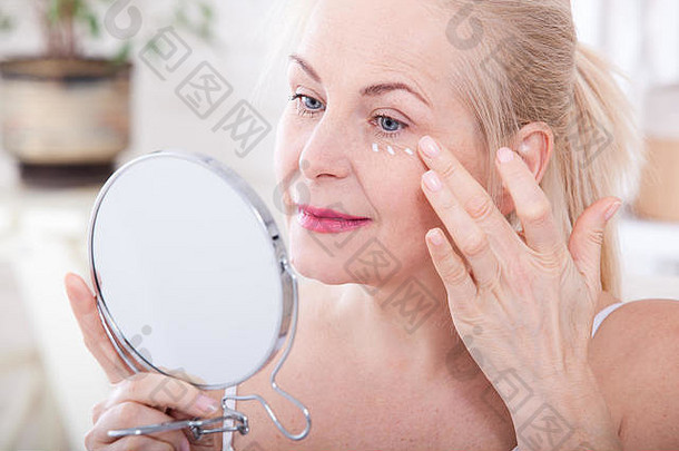 四十岁的女人看着镜子里的皱纹。整形手术和胶原蛋白注射。化妆。宏观面。有选择地聚焦在脸上。具有自身缺陷的真实图像。