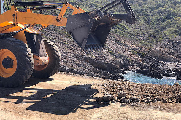 黄色装载机反铲正在道路施工工程期间规划路面。土方、挖掘、岩石土壤上的挖掘。
