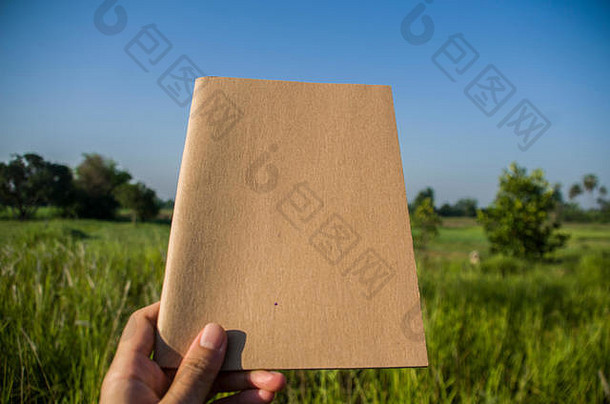 在泰国蒋马的室外花园里，手拿着自然光的棕色笔记本。