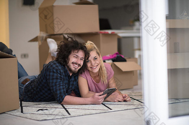 相爱的年轻夫妇搬进新公寓，躺在地板上，在平板电脑上上网，寻<strong>找</strong>新的<strong>装修</strong>创意