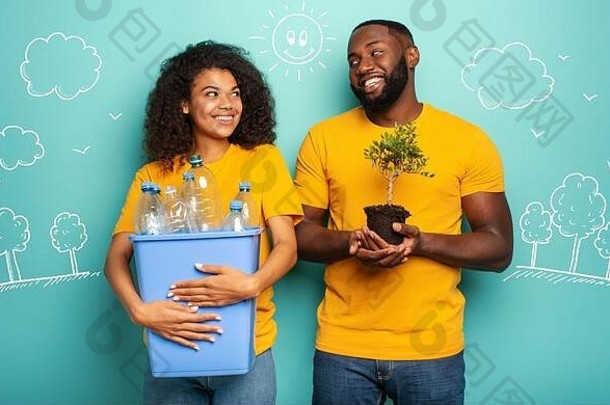 这对幸福的夫妇拿着一个装有<strong>瓶子</strong>的<strong>塑料容器</strong>和一棵浅蓝色的小树。生态、保护、循环利用和可持续发展的概念