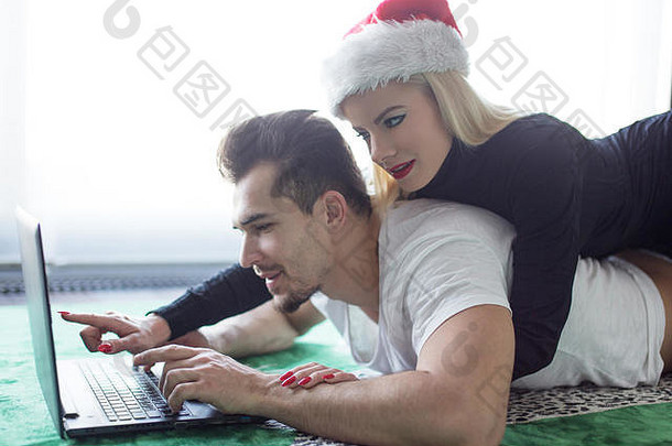 这对年轻夫妇躺在地毯上为圣诞节在线购物