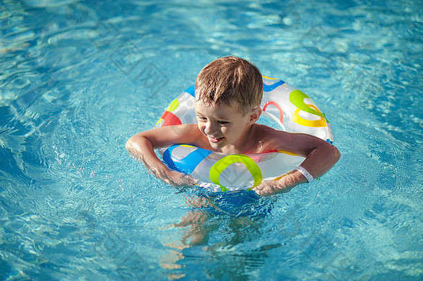 戴着救生圈的快乐男孩在游泳池里尽情地玩耍。