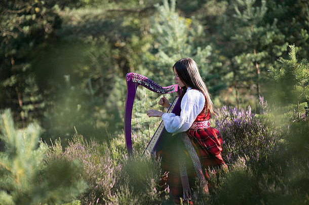 穿着拉脱维亚民族服装的女孩在夏日森林里弹奏着凯尔特人的竖琴