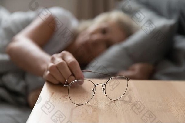 特写镜头聚焦于木制床头柜上的眼镜。