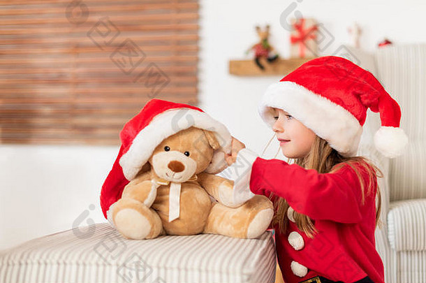 可爱的小女孩戴着圣诞帽，玩着她的圣诞礼物，软玩具泰迪熊。圣诞节时玩得很开心的孩子，带着柔软的玩具。