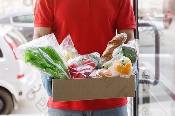 疫情期间从超市交付产品。拿着一箱食品杂货的快递员。