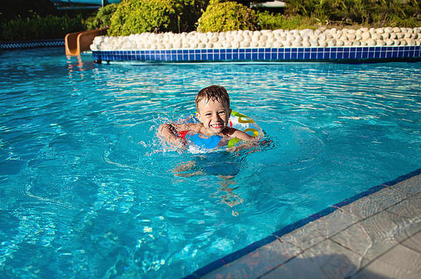 戴着蓝色救生圈的快乐小男孩在游泳池里玩得很开心。进入度假村