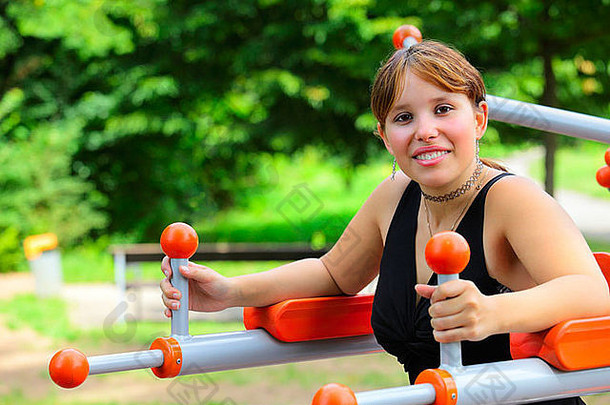 一位<strong>年</strong>轻女子坐在运动设备上，在运动练习之间的停顿<strong>中大</strong>笑。Saarlouis市公园室外，