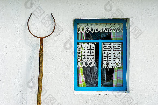 乡村农舍的白色墙壁和蓝色的窗户。窗户左边的烤箱叉
