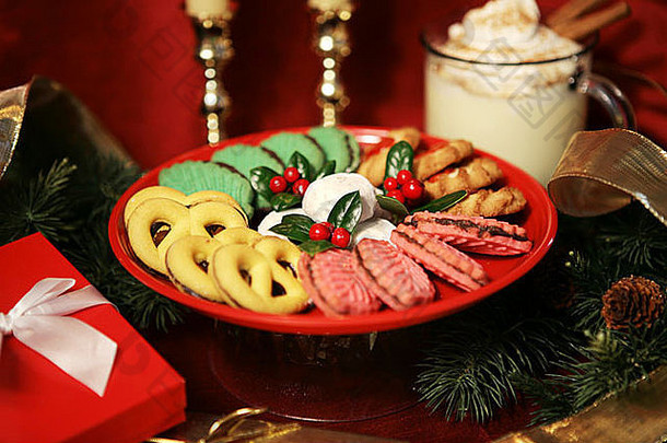 松枝和礼物旁边的桌子上放着一盘漂亮的圣诞饼干和一杯蛋酒