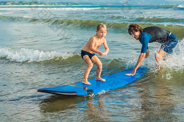父亲或教练在假期或假日教他4岁的儿子如何在海里冲浪。儿童旅游和体育概念。儿童冲浪<strong>课</strong>
