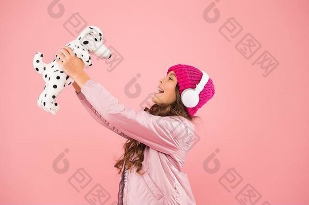 让我们一起玩吧。粉红色是她最喜欢的颜色。小孩子戴着耳机听音乐。儿童长卷发。舒适的冬季。宠物护理。寒冷天气穿暖和的衣服。快乐的小女孩玩狗玩具。