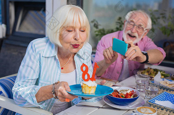 一个拿着生日蛋糕的盘子的积极的老妇人