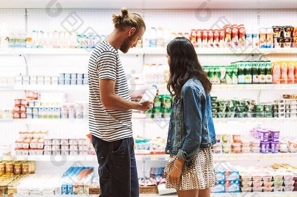 一对年轻漂亮的夫妇在超市乳制品部一起深思熟虑地挑选牛奶