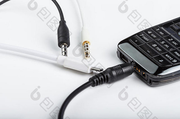 手机配件、插头、耳机、白色背景上隔离的连接器和带键盘的黑色电话