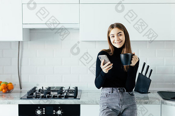 年轻漂亮的女人在厨房里用手机喝<strong>咖啡</strong>