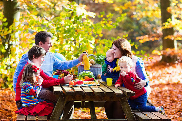 快乐年轻的家庭孩子们烧烤肉使三明治沙拉野餐表格阳光明媚的秋天公园