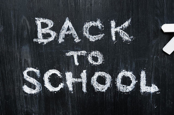 “回到学校”这句话写在黑木头背景上，俯视图。新学期，教育理念：平铺的手写字和粉笔