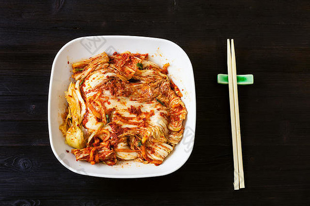 <strong>韩国料理</strong>-白色碗中的泡菜开胃菜（辣味纳帕卷心菜）和深棕色木桌上的筷子的俯视图