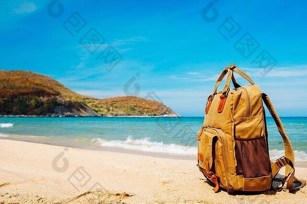 旅游、度假期间，游客可将时尚的棕色背包放在热带海滩的岸边。背景为沙滩、海景和山景。弗里拉